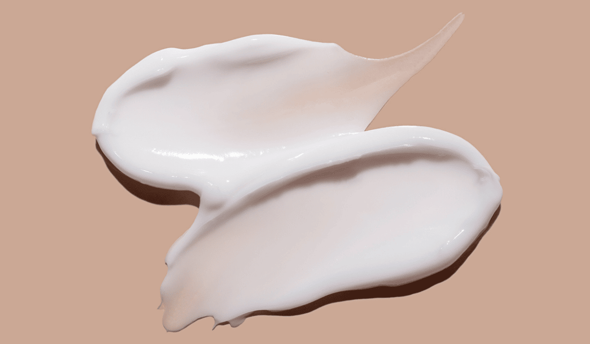 Creamy white cosmetic formulation swatched on a nude background, showcasing smooth and glossy texture