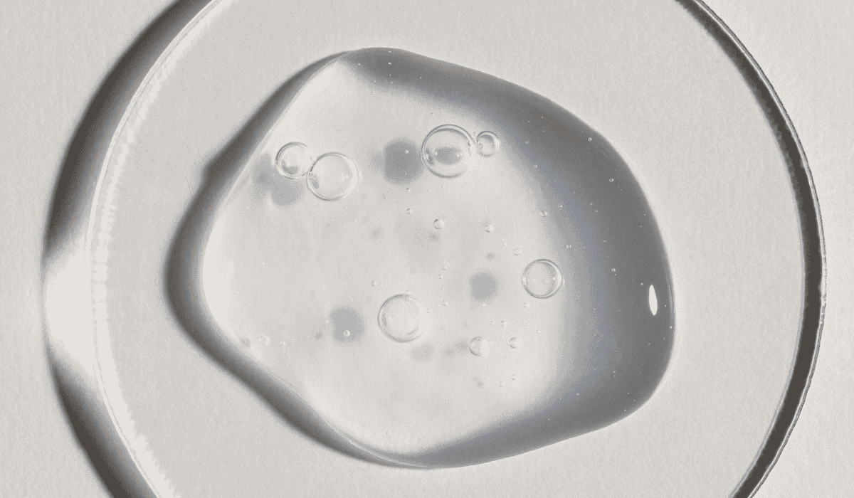 Clear gel texture with air bubbles, viewed on a glass petri dish against a white background — representing a hyaluronic acid or sodium hyaluronate serum.          Ask ChatGPT